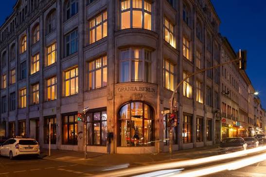 A restored corner building of dark brick facing an open Berlin square