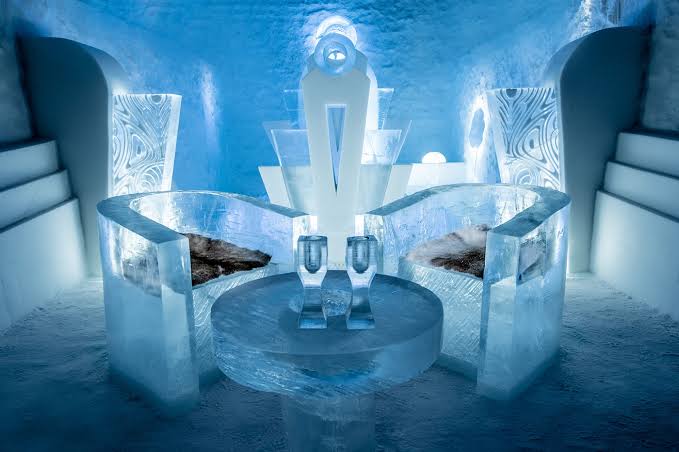 A carved ice chamber lit in pale blue with a block wall behind the bed
